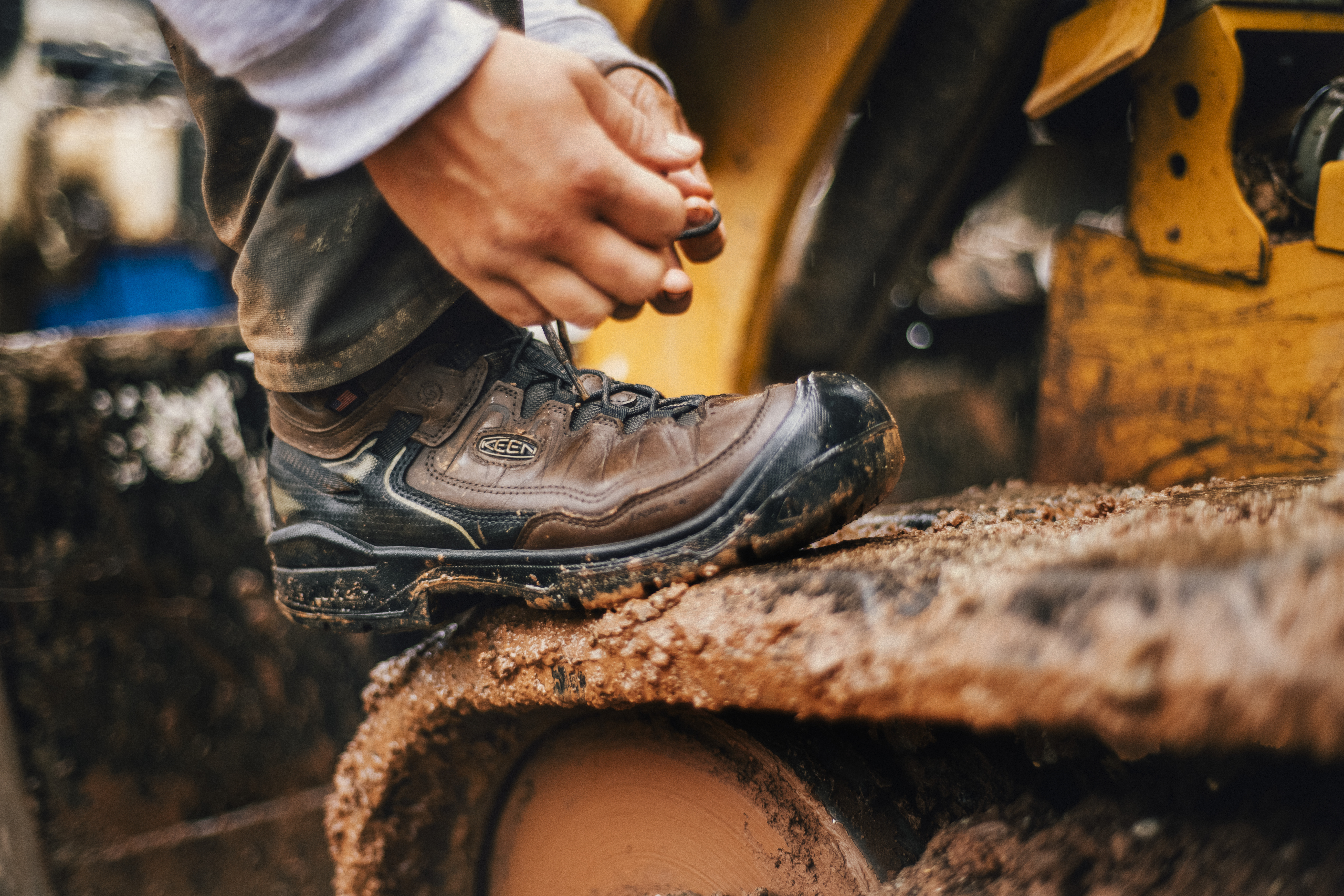 Worker tying a safety boot beside heavy equipment.