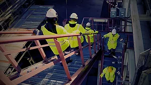 Workers in high-visibility clothing descending stairs in an industrial facility.