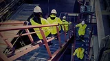 Workers in high-visibility clothing descending stairs in an industrial facility.