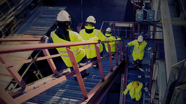 Workers in high-visibility clothing descending stairs in an industrial facility.
