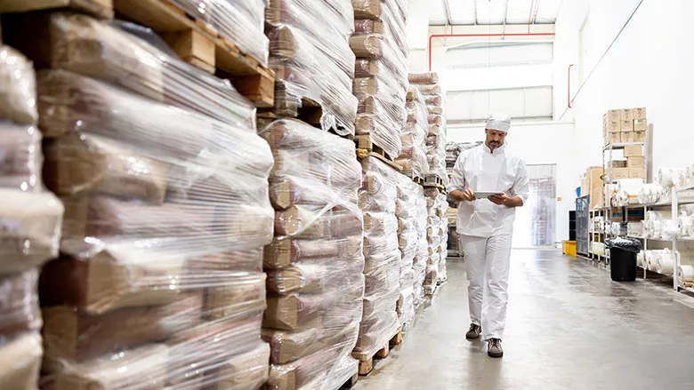 Worker checking inventory in a warehouse aisle.