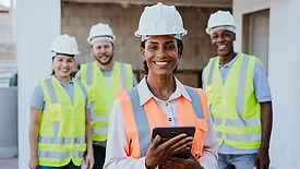 Construction team leader holding a tablet with site crew in the background.