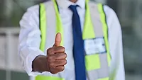 Construction Supervisor Giving Thumbs-Up Construction supervisor giving a thumbs-up while wearing a high-visibility safety vest.