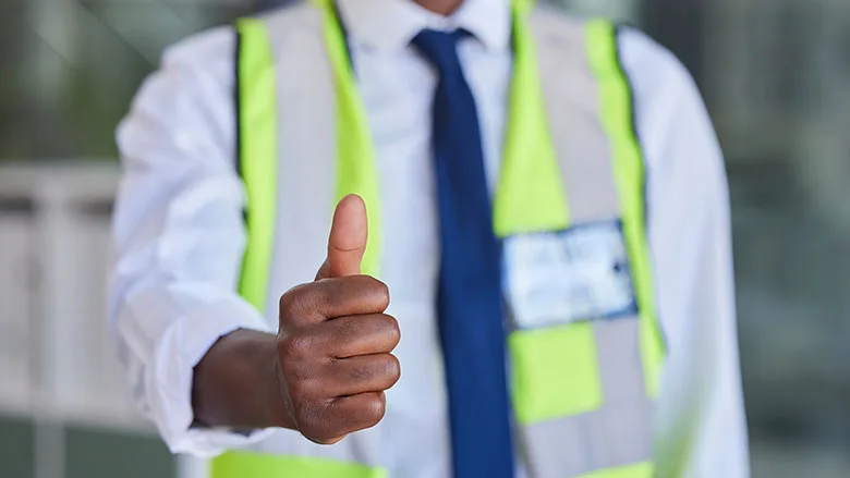 Construction supervisor giving a thumbs-up while wearing a high-visibility safety vest.