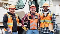 This image shows a group of three construction workers standing in front of a mobile crane. 