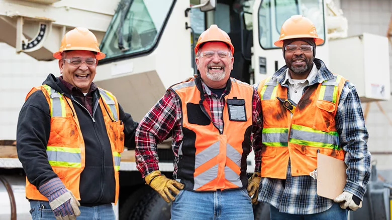 This image shows a group of three construction workers standing in front of a mobile crane.