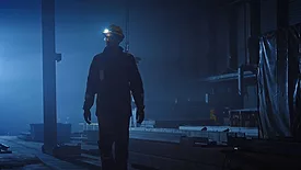 This image captures a scene from a film featuring a industrial worker navigating a dim factory environment. 