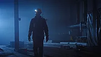 This image captures a scene from a film featuring a industrial worker navigating a dim factory environment. 