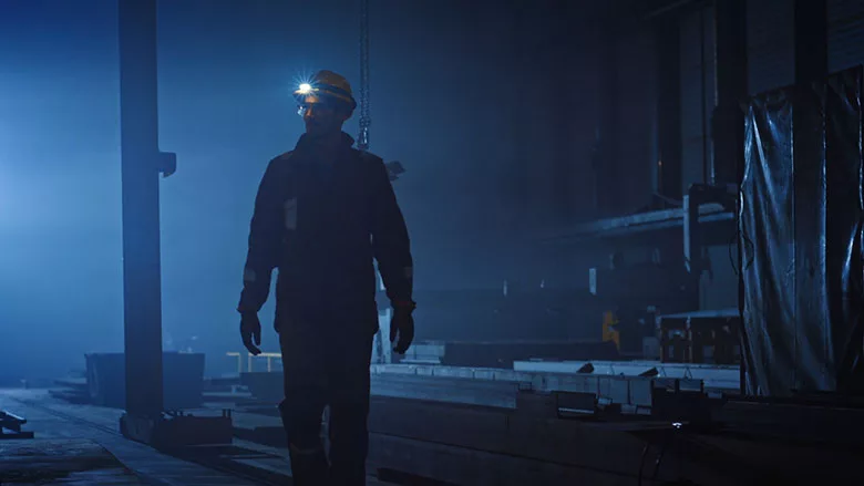 This image captures a scene from a film featuring a industrial worker navigating a dim factory environment. 