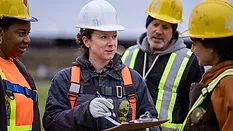This image shows a team of diverse construction professionals reviewing site plans during a workday.