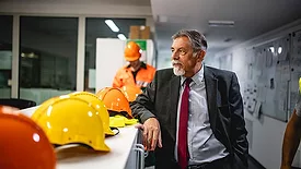 This image shows a man in a business suit overseeing a industrial or construction workplace setting.