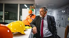 This image shows a man in a business suit overseeing a industrial or construction workplace setting.