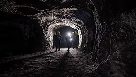 This image depicts a group of miners walking through an underground coal mine tunnel.