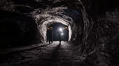 This image depicts a group of miners walking through an underground coal mine tunnel.