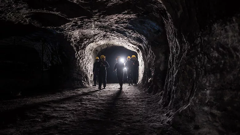 This image depicts a group of miners walking through an underground coal mine tunnel.