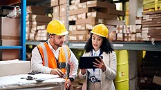 logistics professionals reviewing inventory data on a tablet in a warehouse setting